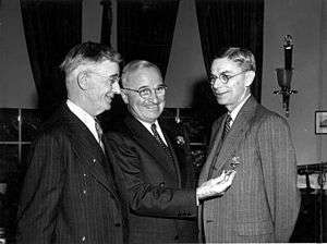 three men in suits. The one on the right is wearing a medal.