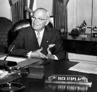 Man in suit sitting behind desk with sign that says "The buck stops here"