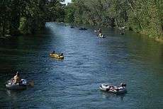 Rafters floating down a midsized river surrounded by forest