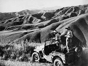 Soldiers in a stationary jeep view steep undulating countryside