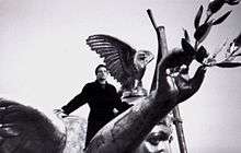 Bono standing atop a large statue of an angel.