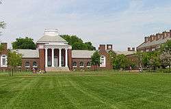 A brick neoclassical building topped by a dome and fronted by four white columns, with a green lawn in the foreground