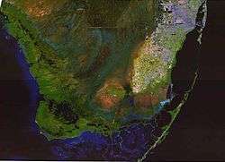 A color satellite image of the southern Everglades, Florida Bay, Atlantic Ocean, and Gulf of Mexico; the Everglades are green with large sections of blue water, with some brown raised areas and the southernmost tip of the South Florida Metropolitan Area in white