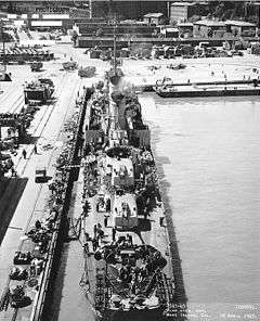 Historic photograph of the USS Wadleigh at dock and under work at the Mare Island Naval Shipyard in 1945. Shipyard buildings are visible in the background.