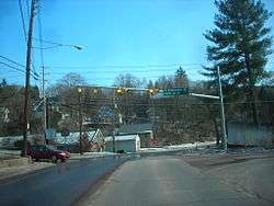 Image of intersection with one car moving in at the left and a few buildings in the distance. There is a stoplight, which is yellow, and a sign which reads "<-- Elizabeth St      Park St -->."