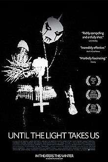 film title, awards and critical commentary imposed over a stark black-and-white image of a man in black metal-wear – black clothing, spikes and corpse paint – holding an inverted cross