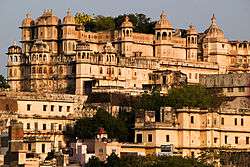 Side view of an ornately decorated palace with several towers on a hill over a city of terraced houses.