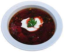 A bowl of dark-red borscht garnished with a dollop of sour cream and a parsley leaf