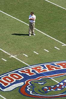 Urban Meyer, standing on the field with his arms folded