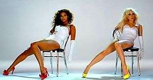 A brunette and a blonde sitting on a chair. Both of them wear white leotards and have a glove on their left hand. The brunette has dark skin and wears red heels. The blonde looks to the left and has yellow shoes on her feet. The background is white.