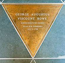 A golden triangular marker set amidst triangular green stone tiles. Engraved on it is "George Augustus Viscount Howe" in large type, and in smaller type below "Is buried beneath this pavement ... Killed near Ticonderoga July 6, 1758"