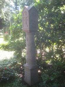 A gravestone in the shape of a column, surrounded by foliage