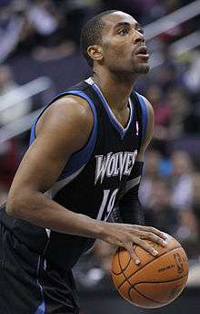 Wayne Ellington with a goatee and a Shape-Up hair style, wearing a black Timberwolves uniform with blue and white trim with a basketball
