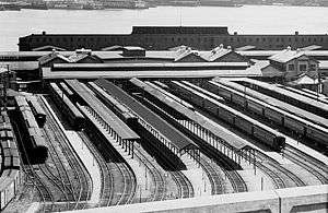 Black & white picture showing station facility with passenger cars. Hudson river visible behind the station.