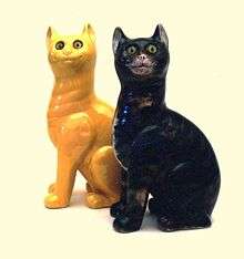 A black ceramic cat sits next to a yellow ceramic cat.