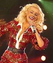 Aguilera wearing a red outfit performing with a microphone and smiling