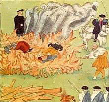 Three people lie on a large fire, watched by several men.