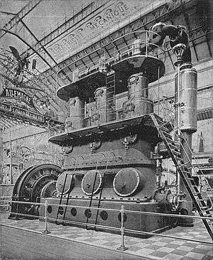 A large three-cylinder stationary steam engine, driving a dynamo generator. The engine is so tall that there are two gallery walkways around it at different heights, with ladders between them.