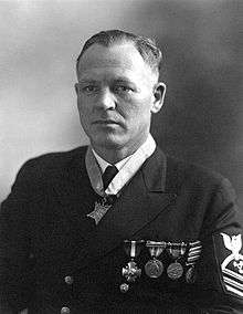 Head and shoulders of a white man wearing a dark jacket with four medals on the left breast and a star-shaped medal hanging from a ribbon around his neck.