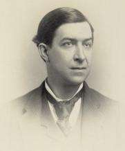 A man in his late thirties with short, black hair wearing a black jacket and tie and white shirt