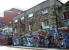 A three-storey stone-faced building. The first level is decorated with colourful graffiti.