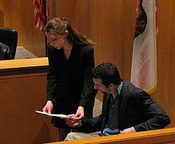 A woman and a man reading a document in a courtroom