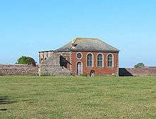 A small brick Neoclassical chapel with a slate roof, and part of a loggia behind
