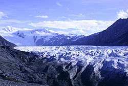 A glacier, mountains of black gravel and snowcovered mountains.
