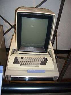 A beige, boxy computer with a small black and white screen showing a window and desktop with icons.