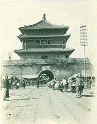 An old black and white picture of the Bell Tower with a lot of Chinese people in traditional clothes.