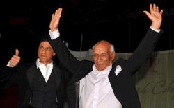 Two men, the older one with arms raised and the younger one making a thumbs-up sign