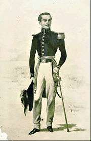 Printed full-length drawing of a thin young man standing and wearing a military tunic with an epaulet on the left shoulder, white trousers and his left hand resting on the hilt of a sword worn at the waist and his right hand holding a plumed hat