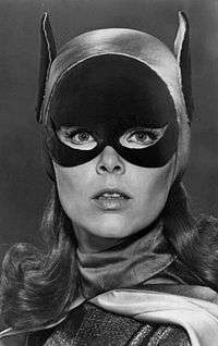 A black-and-white portrait of Yvonne Craig as Batgirl, wearing a mask that covers the top half of her face, though with eyes and nose exposed.  She is also wearing a hood that has bat-like ears extending up on each side of her head.