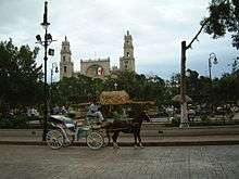 Scene of a plaza, with a horse and carriage in the foreground.
